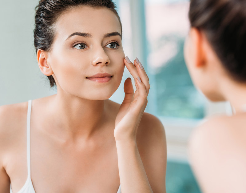woman looking at herself in the mirror focusing on facial skin care